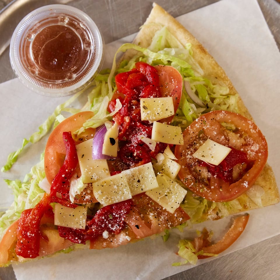 A slice of Napoli's Pizza with lettuce, tomatoes, red peppers, onions, and cheese, with dressing.