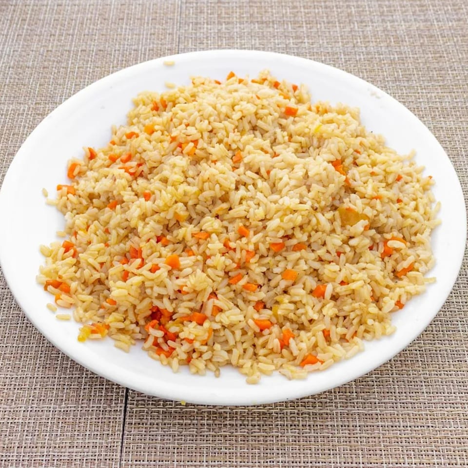 A white plate filled with golden brown rice and diced orange carrots on a woven placemat.