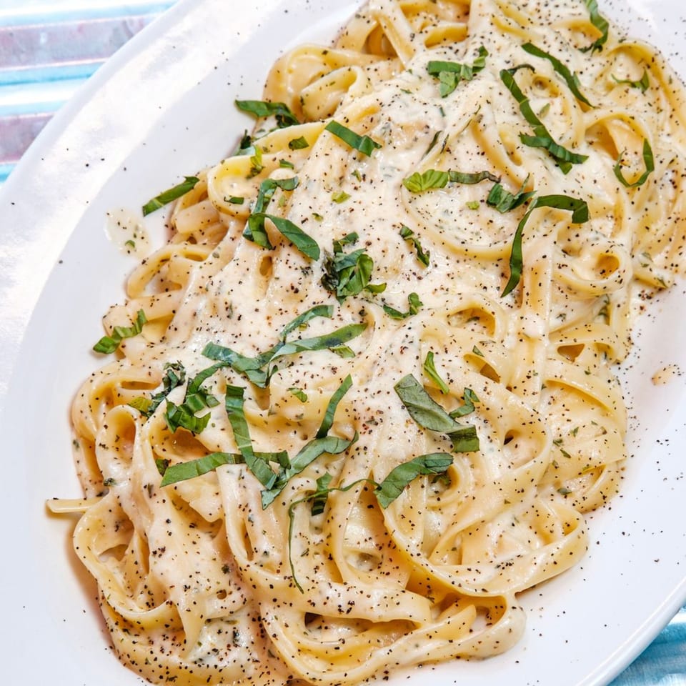 Creamy fettuccine alfredo with fresh basil and black pepper on a white rectangular plate.