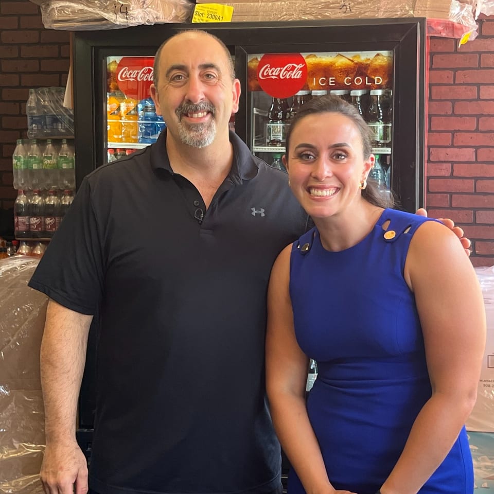 Two smiling Napoli's Pizza & Catering staff members stand in front of a Coca-Cola cooler.
