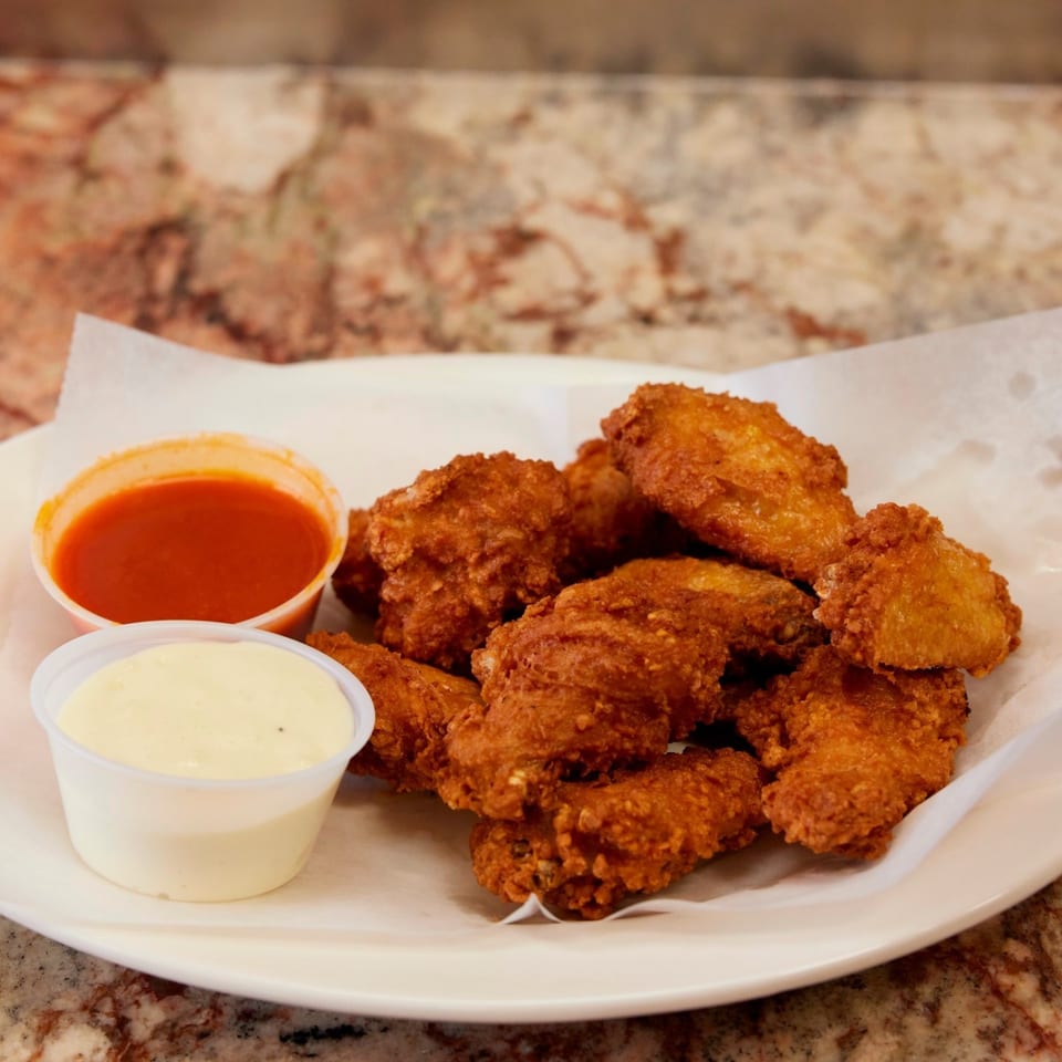 Crispy fried chicken wings with two dipping sauces, red and white, on a white plate.