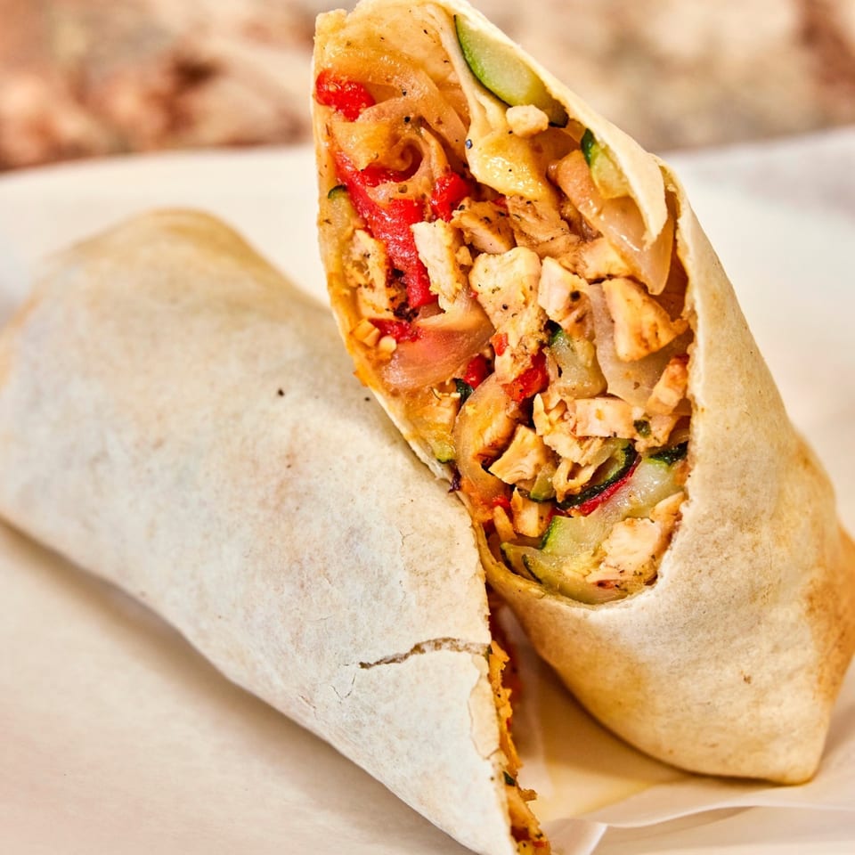 Two chicken shawarma wraps, one cut in half, revealing chicken, red peppers, and cucumbers.